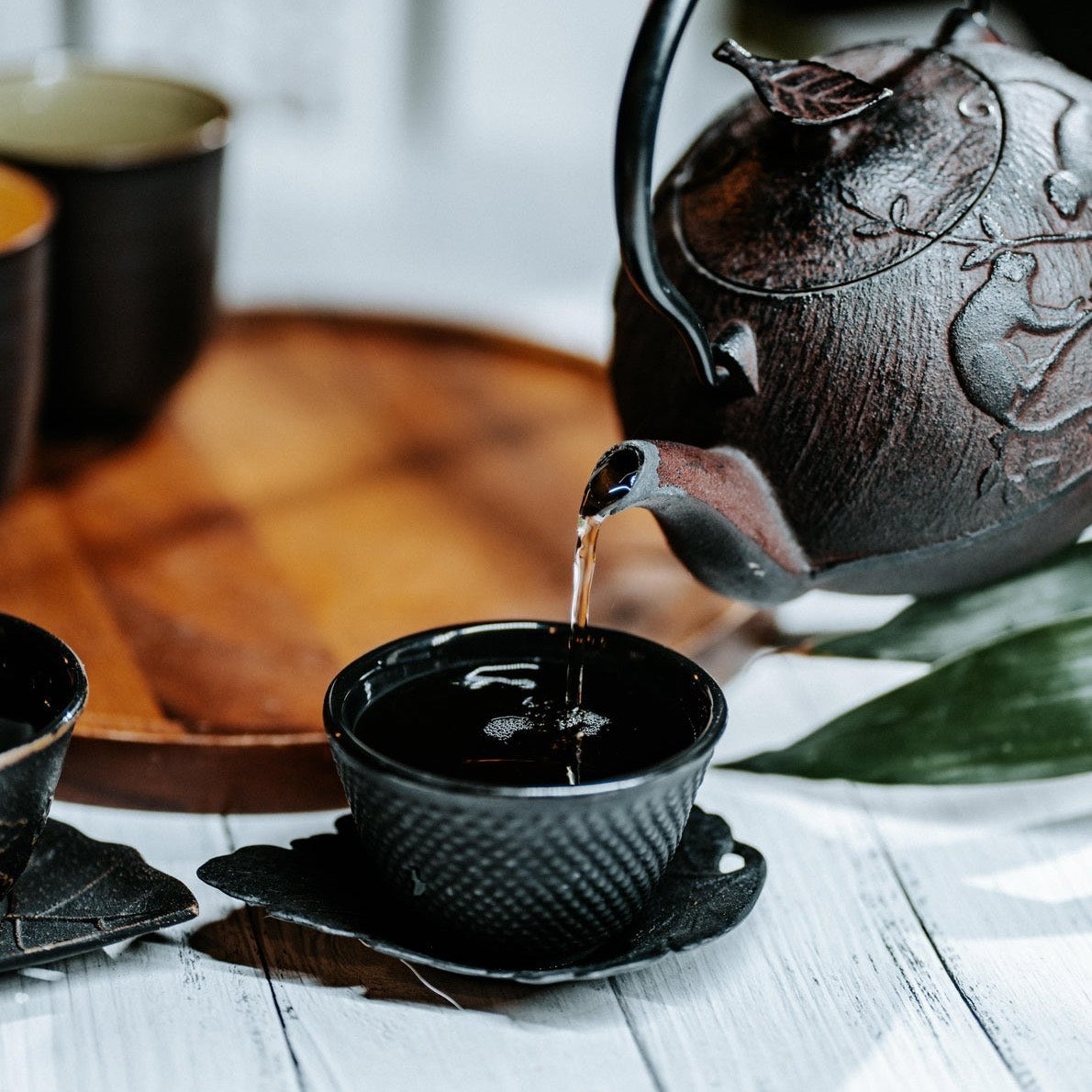 Tea being poured from a cast-iron teapot into a small black cup